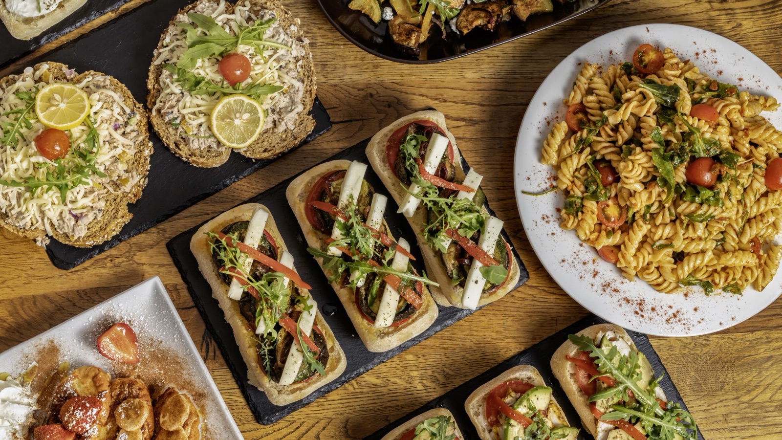 A wooden table spread with fresh sandwiches, bruschetta, pasta salad and small plates at The Barrel Boulangerie.